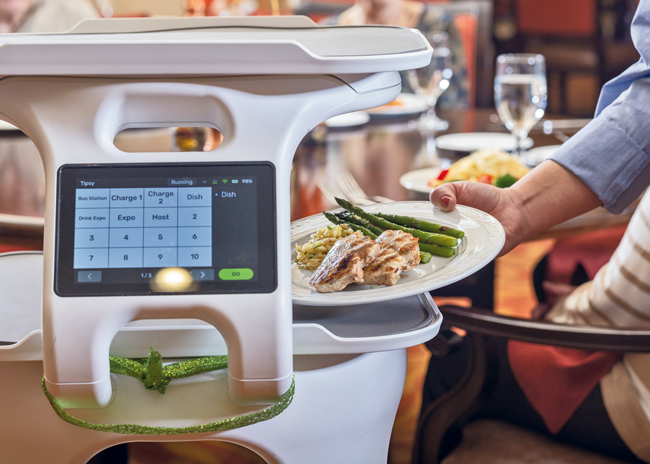 In the dining room at Providence Point,  a robot is used to bring food to tableside for servers to distribute to individual diners. Another robot is used to bus dirty plates to the dish room. Photos courtesy of Cura Hospitality