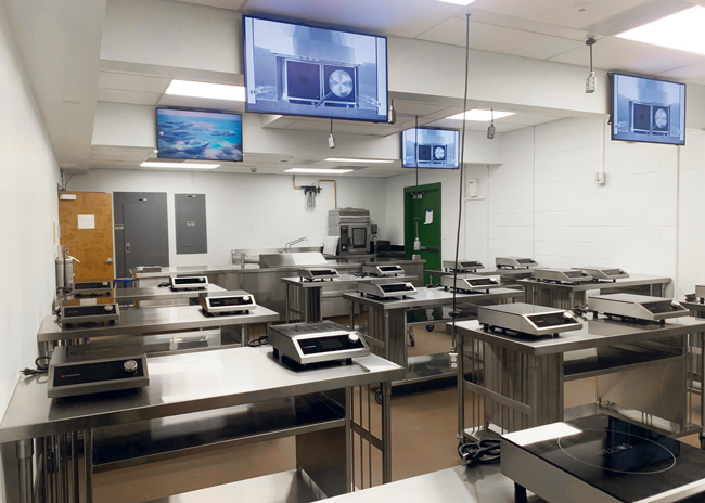  Students watch overhead monitors that mirror the instructor’s counter for visual learning. 